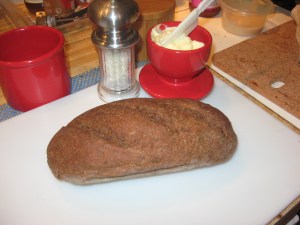 One loaf of pumpernickel bread on cutting board with butter-bell